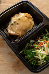 A view of a black container, featuring caper chicken, and a salad.