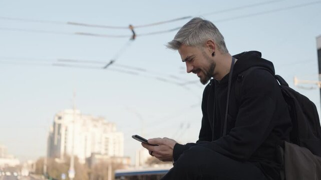 Happy man with silver hair outdoors, smiling while actively using his smartphone in the city.
