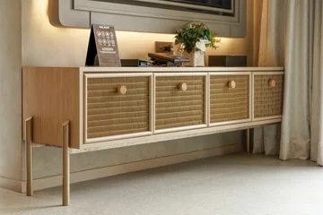 Fototapete Japandi Modern wooden media console or TV stand with woven rattan drawers and matching knobs. Japandi style furniture in a contemporary living room with soft ambient lighting in the background.  © Okta