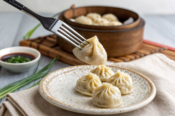 shows a plate of steamed dumplings with a fork holding one up, surrounded by green onions, a bowl of dipping sauce, and a wooden steamer basket filled with more dumplings in the background.