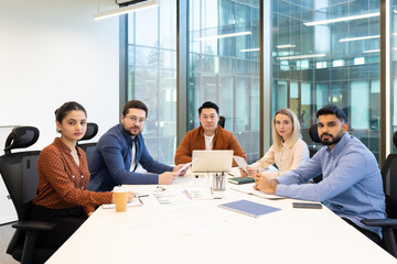 Diverse group of business professionals in a modern office setting, gathered around a table during...