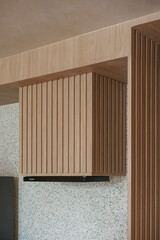 Architectural detail of a modern kitchen range hood concealed by fluted light oak paneling, set...