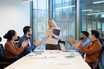 A diverse team applauds their colleague in an office setting, celebrating success and teamwork.