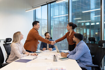 A diverse group of business professionals are shaking hands at a meeting table in a modern office.