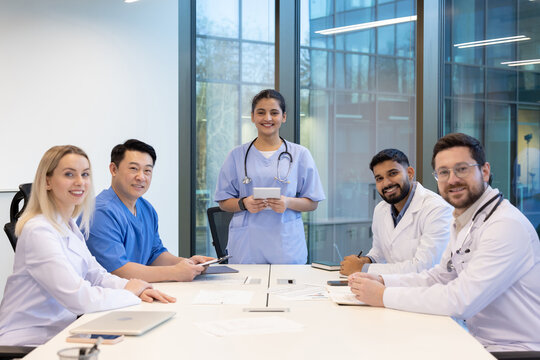 A team of diverse medical professionals is gathered around a table in a modern office setting, smiling at the camera.