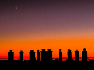 coucher de soleil sur les toits d'une ville sous une lune ascendante dans son premier quart, éclairant les cheminées des immeubles