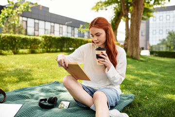 Young woman enjoying a quiet afternoon in the park while sipping coffee and reading a book