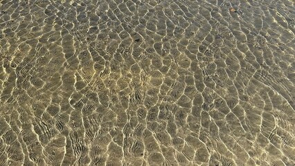 Shimmering clear water in shallow river, sun reflection, sunny summer day, sandy bottom. Horizontal yellow background.