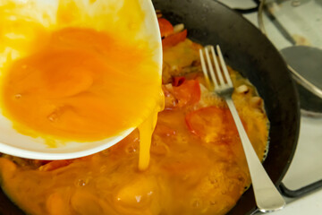 pouring beaten eggs into frying pan with vegetables for Hungarian lecsó