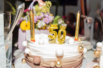 
Elegant 50th Birthday Cake With Golden Number Candles And Crown Decorations On White Frosting...