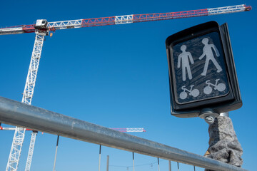 Urban pedestrian sign with figures crossing on black background and cranes behind, merging urban infrastructure, construction, and city travel routes as part of modern travel narratives