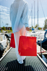 Young female holding a red shopping bags during sunny day with blue sky background