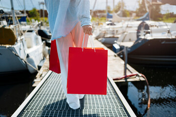 Young female holding a red shopping bags during sunny day with blue sky background