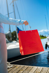 Young female holding a red shopping bags during sunny day with blue sky background