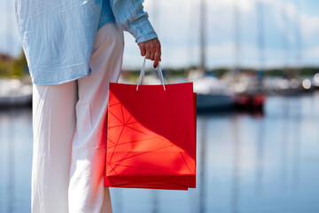 Young female holding a red shopping bags during sunny day with blue sky background