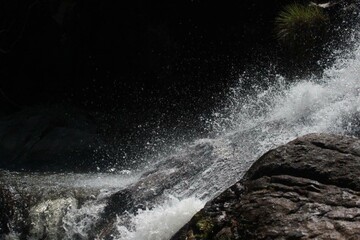 Close-up shot of a waterfall cascading over dark rocks in a tropical forest in Thailand. Water...