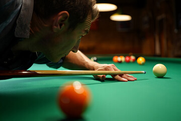 Close-up of a pool player aiming cue at white ball on green table, capturing focus and precision in mid-shot.