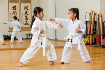 Children practice karate in a bright dojo, wearing white uniforms and colored belts, performing synchronized punches.