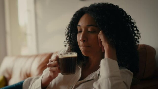 a woman with curly hair, sitting on a couch, drinking coffee in a well-lit room.  The background suggests a warm and inviting. Laptop. 