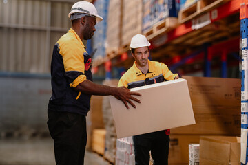 Warehouse manager, store inspector checking stock on storage shelf from inventory checklist. Two diverse ethnic people wear safety hard hat working together examining merchandise at distribution store