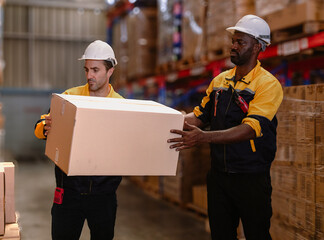Warehouse manager, store inspector checking stock on storage shelf from inventory checklist. Two diverse ethnic people wear safety hard hat working together examining merchandise at distribution store