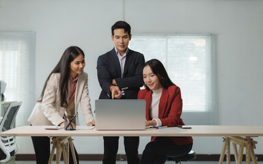 Three colleagues gather around a laptop, discussing and collaborating on a business project in a...