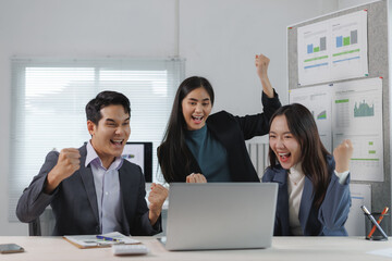 Euphoric businesspeople are cheering and raising their fists while looking at a laptop, celebrating...