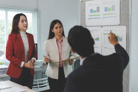 Business team engaged in discussion, analyzing charts on a board in a modern office setting, emphasizing teamwork and data driven decision making