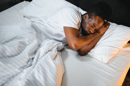 african American man sleeping in comfortable white bed seeing good pleasant dreams, calm biracial male feel fatigue resting napping in cozy bedroom under linen bedding sheets