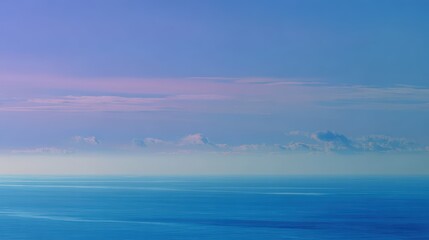 Calm blue ocean merges with the sky under pastel pink clouds at horizon.