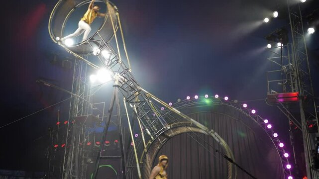 Two brave male acrobats in a rotating wheel of death perform under the dome of the circus in the light of bright concert lights and smoke. A dangerous acrobatic act on a rotating wheel. A circus act.
