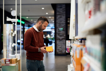 Man Examining Product Packaging in a Modern Pharmacy Setting