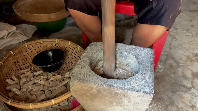 jarak dekat, seorang pria yang sedang menumbuk, dengan lesung batu dan kayu tradisional