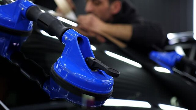 A close-up of the windshield repair process in a car service, blue professional suction cups are visible on the glass. The master applies glue.