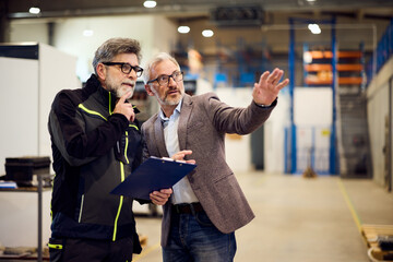 Two Professionals Discussing Work In An Industrial Warehouse Environment