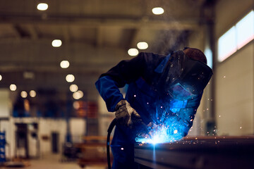 Professional Welder Working in Industrial Workshop with Protective Equipment