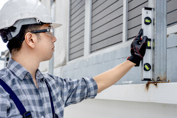 Asian male construction worker using level tool on fence. Home builder man checking the vertical plane of steel column. Measuring tool for building measurement and inspection