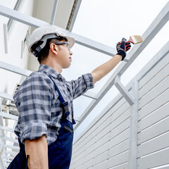 Asian man painter painting white acrylic color on steel beam of roof structure. Male decorator...