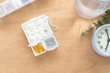 Dietary supplement tablets in plastic box with compartments, water bottle, clock on wooden...