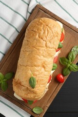 Tasty sandwich with mozzarella cheese, tomatoes and basil on black wooden table, top view