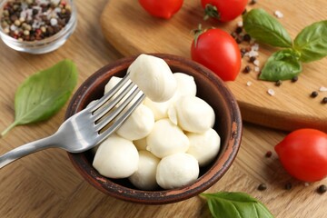 Tasty mozzarella balls, tomatoes, peppercorns and basil on wooden table, closeup