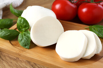Tasty mozzarella, tomatoes and basil on wooden table, closeup