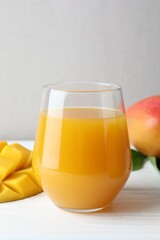 Tasty mango juice in glass and fresh fruits on white wooden table, closeup