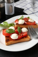Tasty sandwiches with mozzarella cheese, tomatoes, basil and fork on black table, closeup