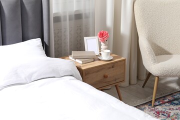 Bedside table with coffee, books and decor near bed indoors