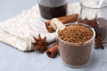 Granulated instant coffee in measuring cup and spices on grey table, closeup