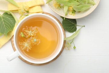 Fresh linden tea in cup and flowers on white wooden table, flat lay. Space for text