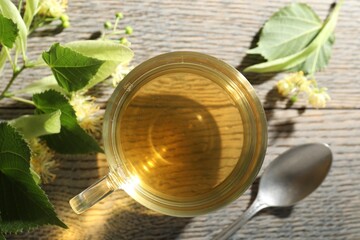 Fresh linden tea in cup and flowers on wooden table, flat lay