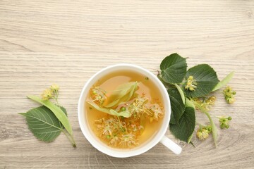 Fresh linden tea in cup and flowers on wooden table, flat lay. Space for text