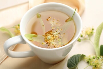 Fresh linden tea in cup and flowers on white table, closeup